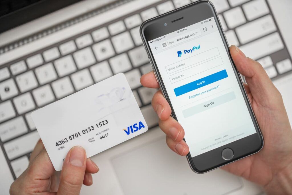 Pessoa segurando cartão visa com o aplicativo do Paypal aberto em seu celular.