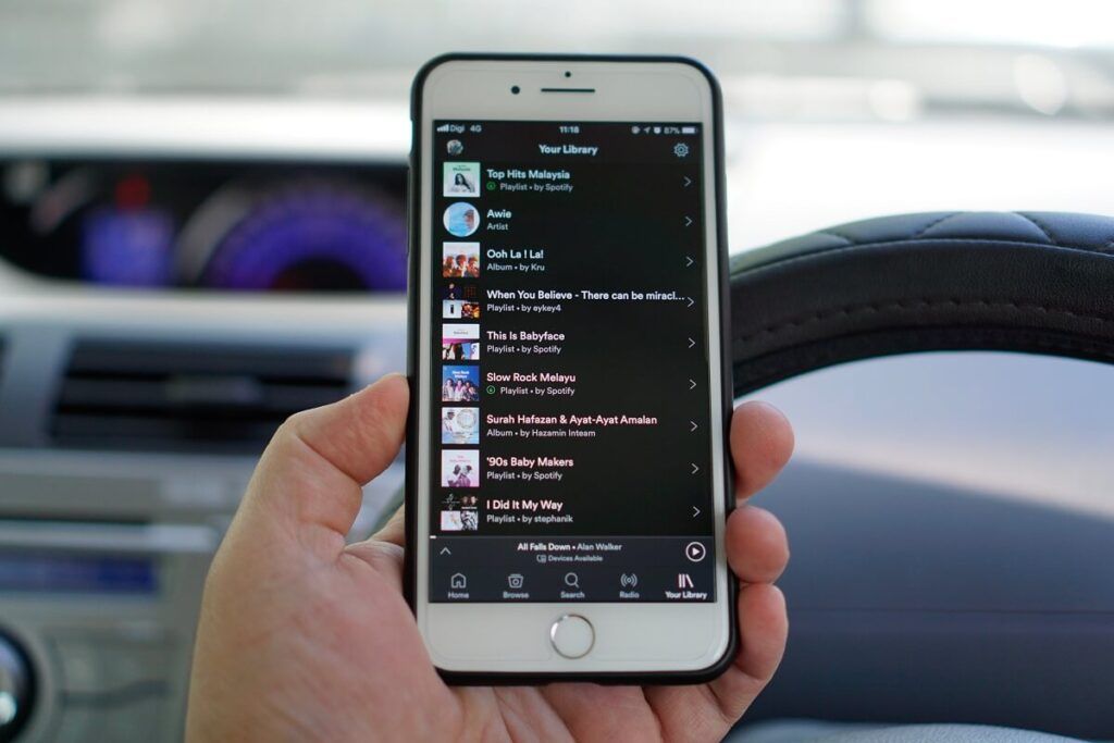 Uma mão segurando o iPhone 7 plus com aplicativos Spotify em um carro