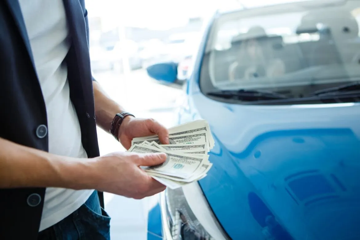 Homem com notas de dólares na mão em uma concessionária de automóveis penando em como comprar carro nos Estados Unidos.