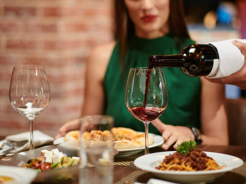 Garçom enchendo taça de vinho da cliente