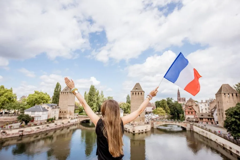 Mulher de braços abertos com bandeira da França comemorando os feriados na França.