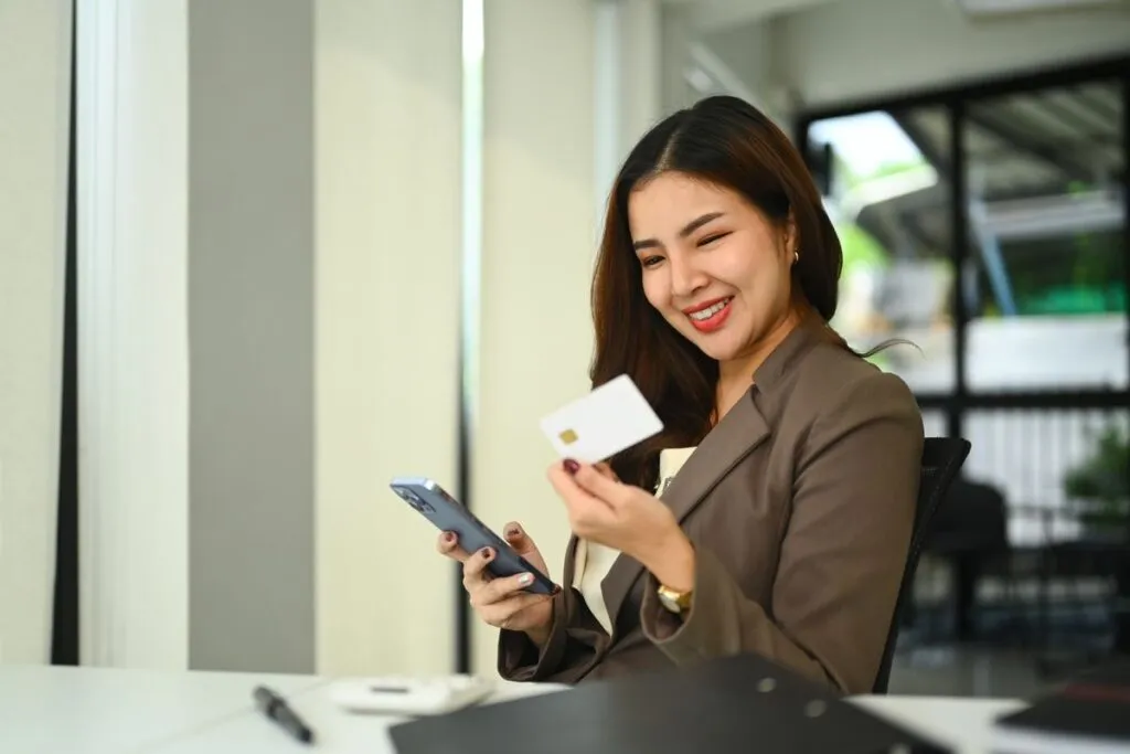 Mulher sorrindo no escritório segurando o cartão do PJBank. 