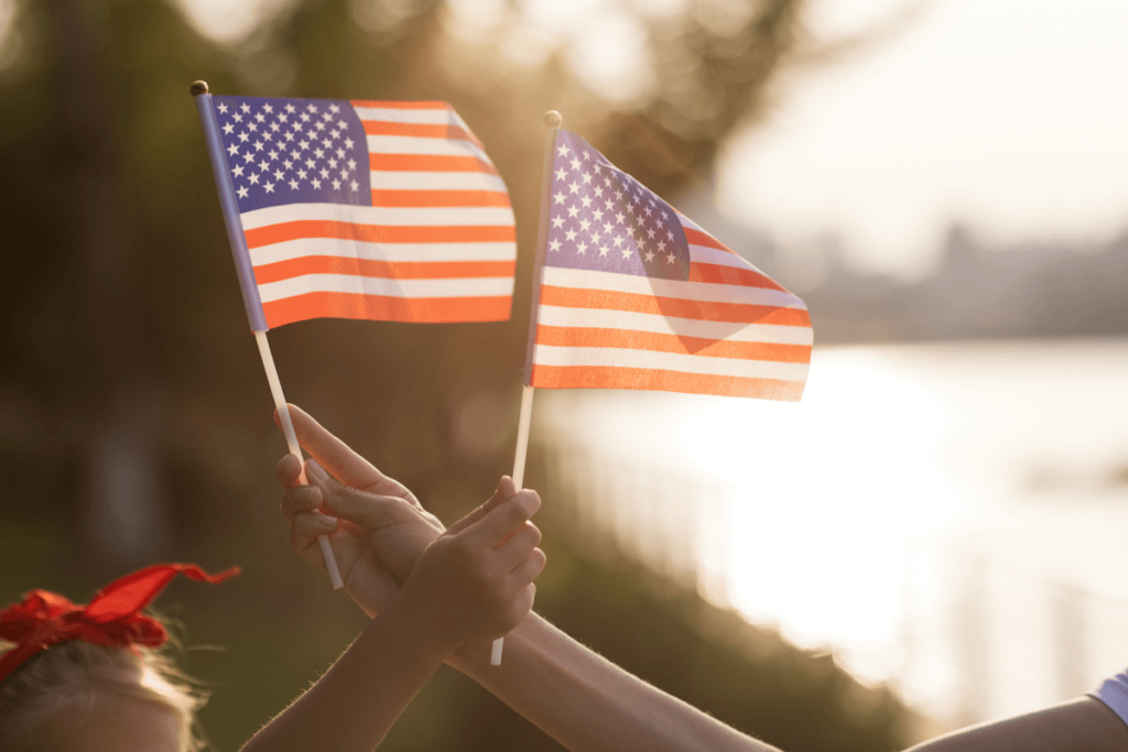 Foto de duas mãos segurando e balançando pequenas bandeiras dos Estados Unidos