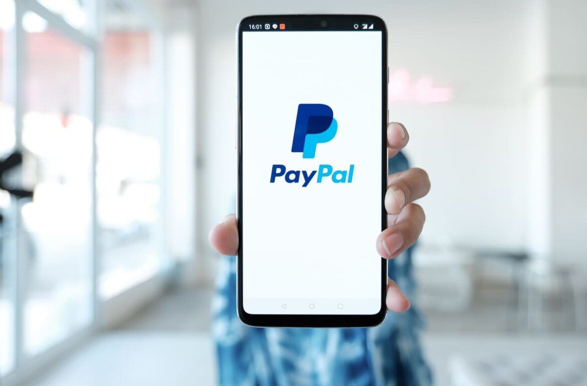 Mão segurando telefone com aplicativo do PayPal aberto