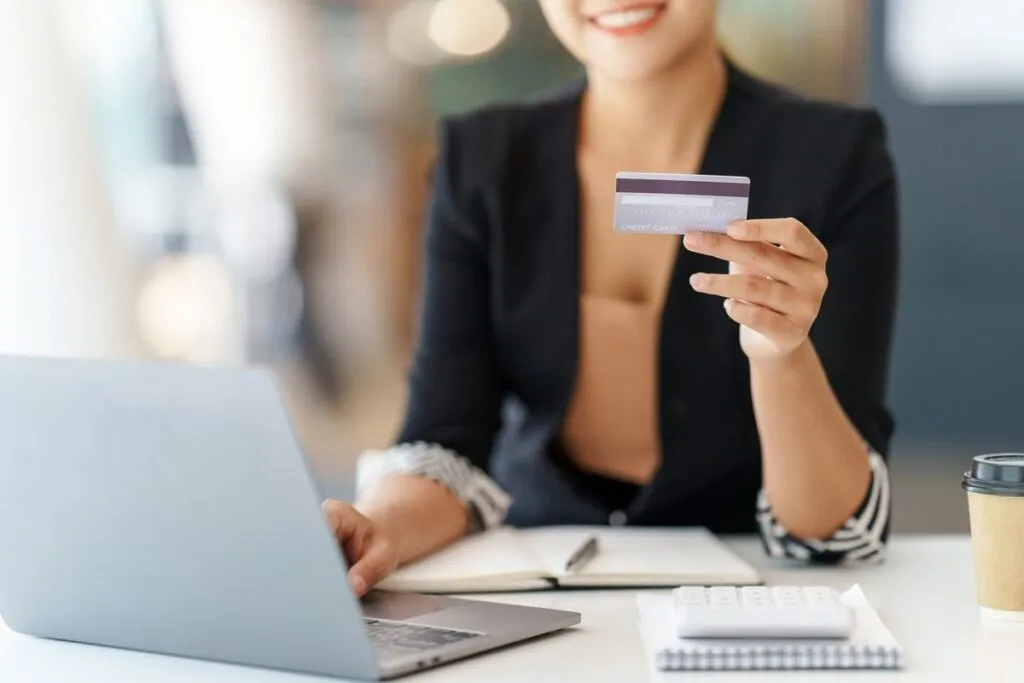 Mulher em escritório segurando o cartão de crédito e usando o notebook