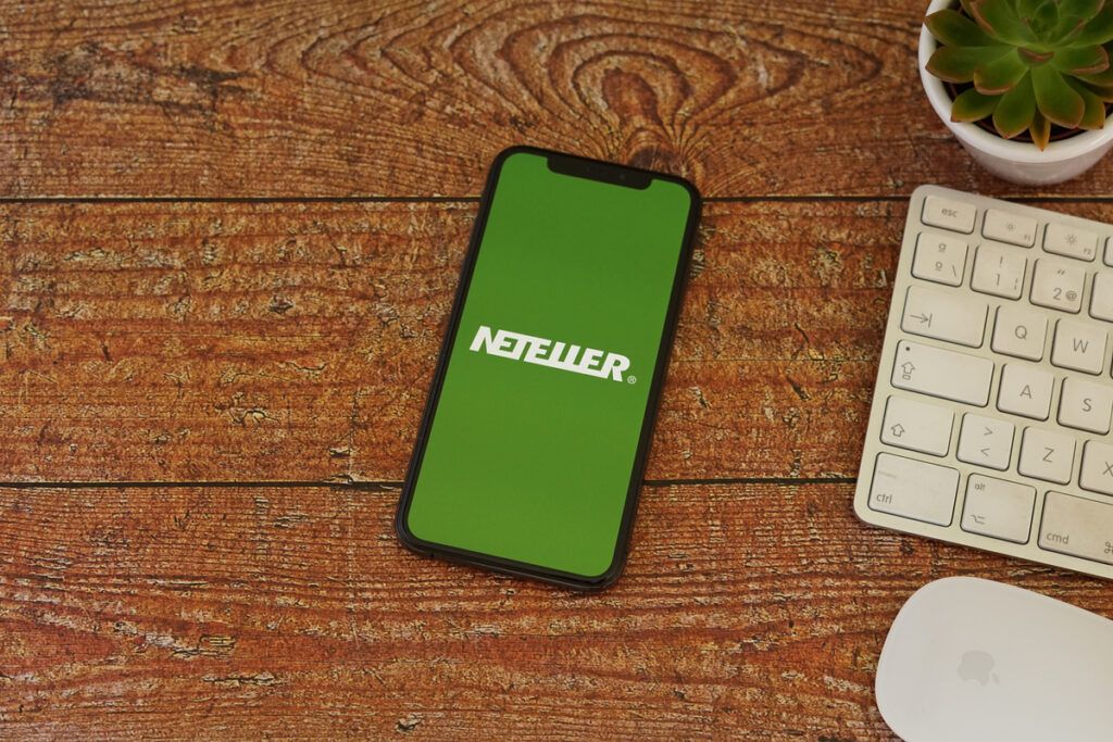 celular aberto na plataforma Neteller ao lado de teclado e mouse 