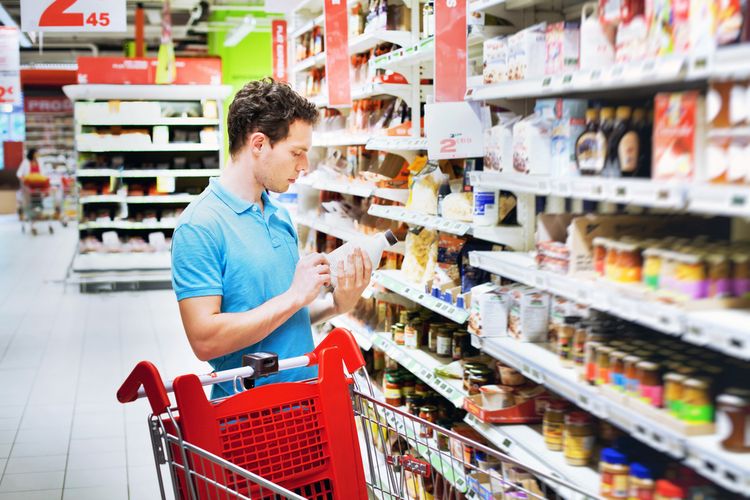 Foto de homem em corredor de supermercado observando o rótulo de um produto
