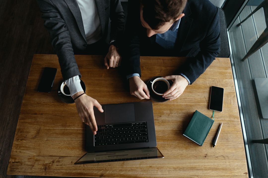mitos e verdades sobre o empreendedorismo - Dois homens sentados, mexendo em um notebook sobre a mesa.