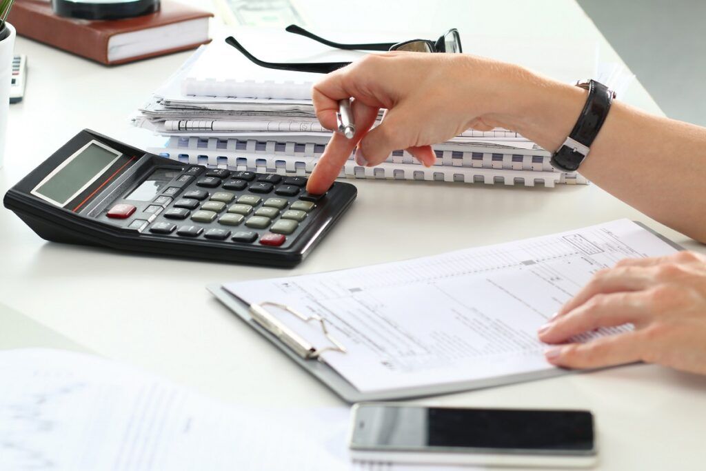 Uma pessoa digitando em uma calculadora, em uma mesa cheia de papéis e documentos
