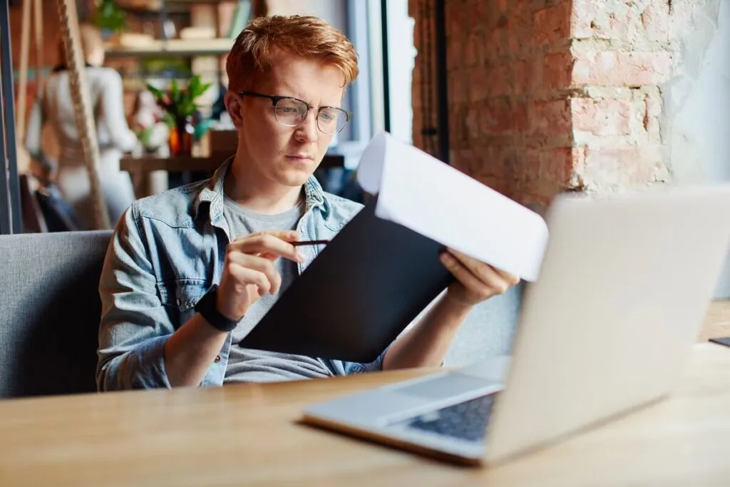 Homem analisando o comprovante de rendimento em uma mesa com um notebook na sua frente