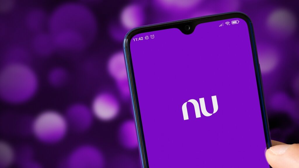 Imagem em primeiro plano da tela de um smartphone exibindo o aplicativo Nu, do Nubank, na mão de uma pessoa.