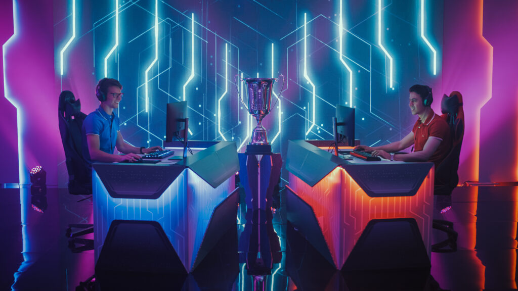 Prêmio esports Dois jogadores de esports sentados em suas mesas de jogo com uma taça entre eles