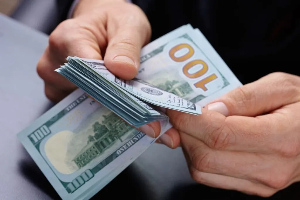 Uma mão branca masculina com dólares simbolizando as vantagens de receber dinheiro do exterior como PJ pela Remessa Online.