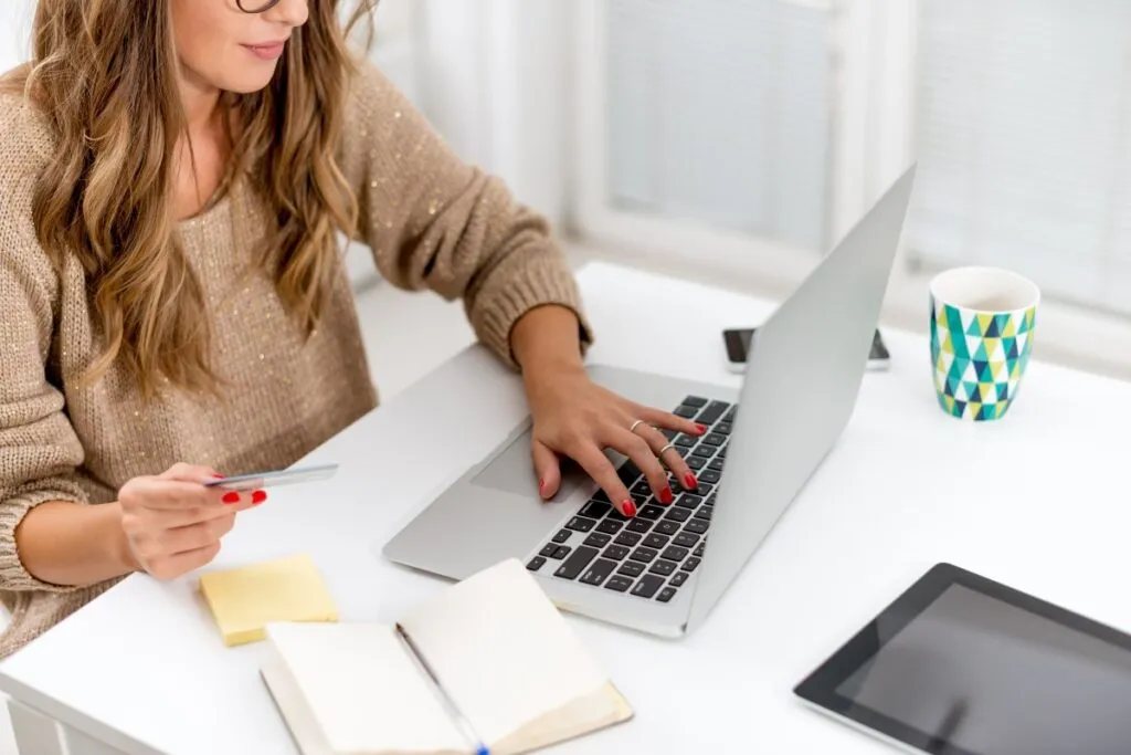 Mulher segurando o cartão de crédito e acessando o notebook