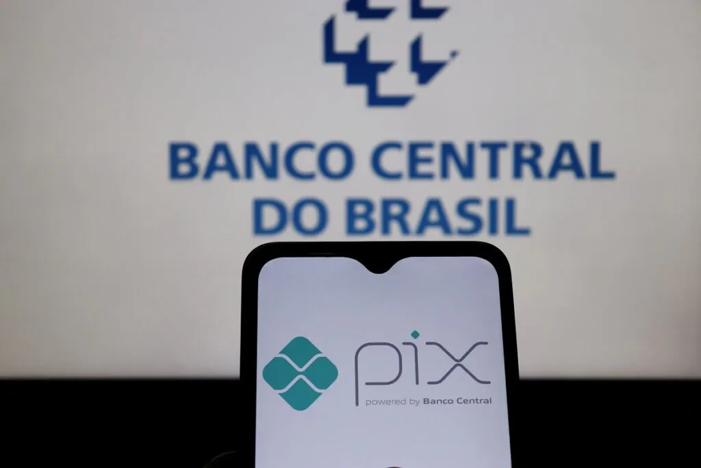 Em um celular mostra o logo do Pix e ao fundo o logo do Banco Central do Brasil