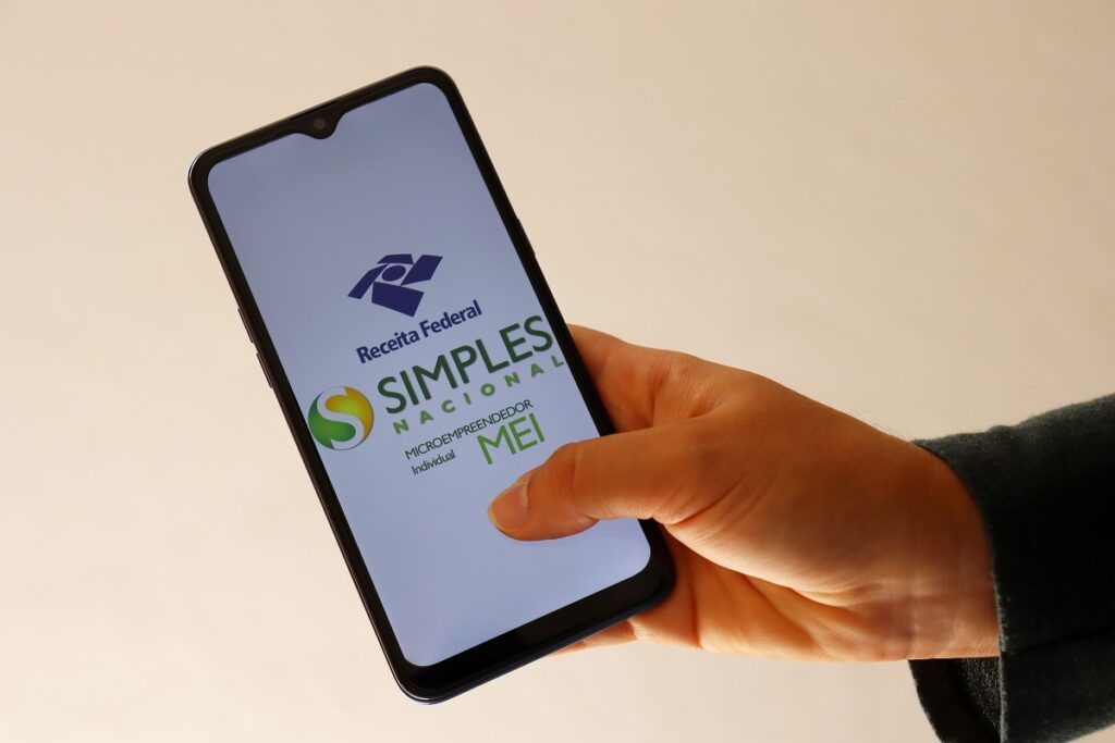 Uma mão segurando um smartphone acessando a página do Simples Nacional