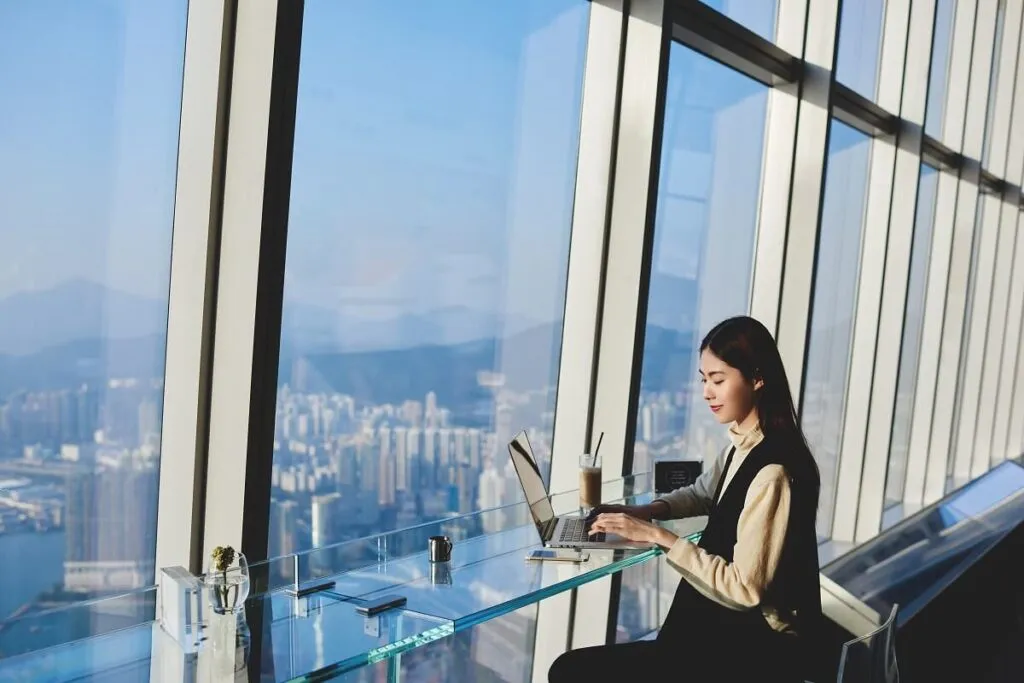 Mulher trabalhando em computador laptop durante sua viagem de negócios para a China, enquanto sentado em um café em arranha-céu perto da janela com vista para a cidade metropolitana