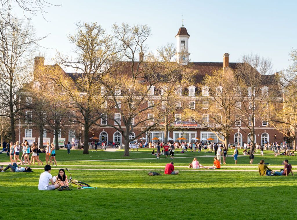 Muitos estudantes em um imenso gramado em um campus universitário.