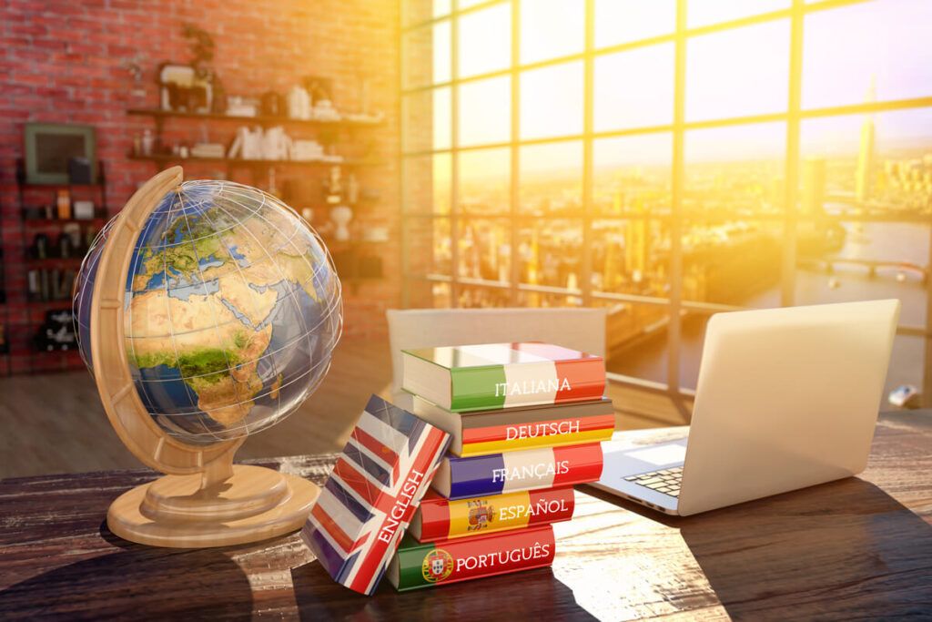 Mesa com globo terrestre, notebook e dicionários de idiomas variados.