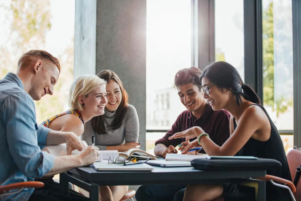 5 estudantes felizes com livros sobre a mesa.