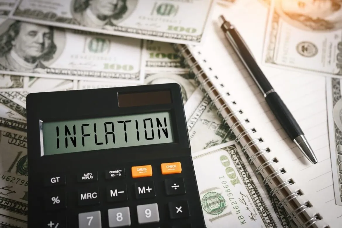 Calculadora escrito Inflation em cima das notas de dólar e uma caneta em cima do caderno