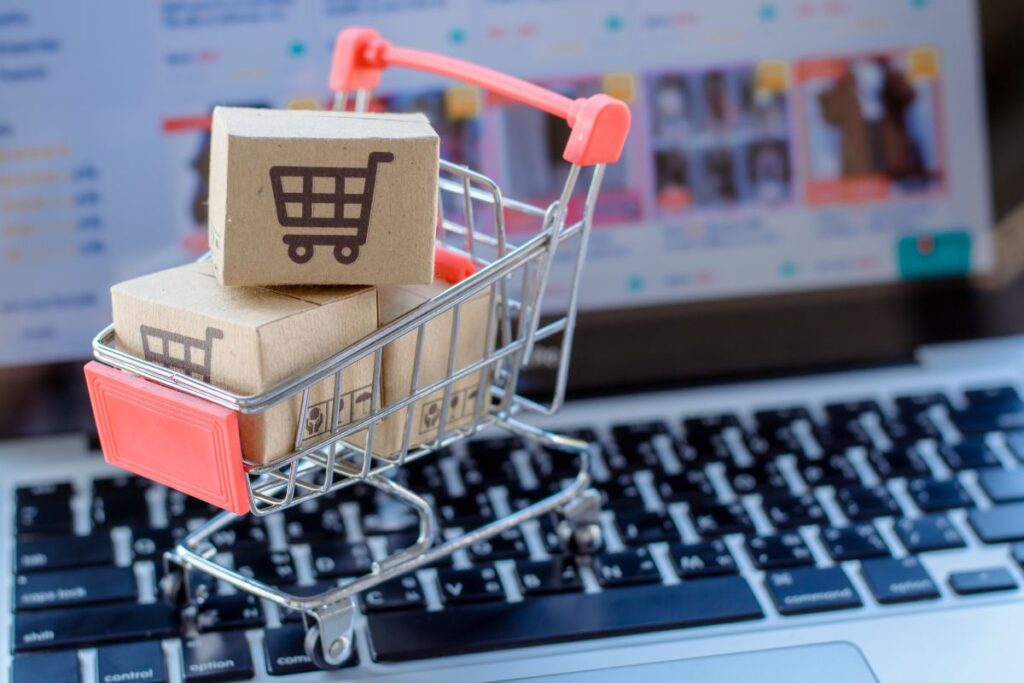 Carrinho de compras com notebook com e-commerce ao fundo.