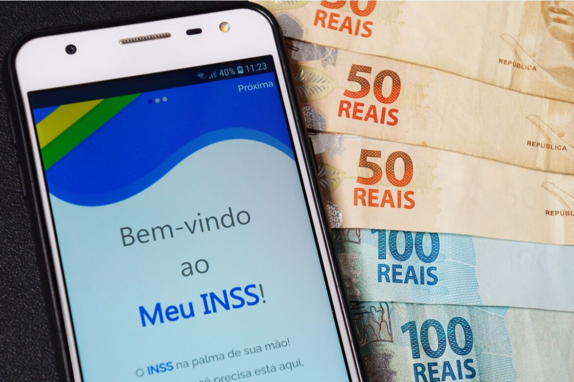 Um celular acessando o site do INSS com notas de 50 e 100 reais espalhadas ao redor