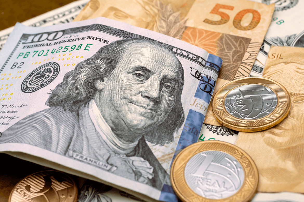 Notas de dólar e moedas de Real em cima da mesa