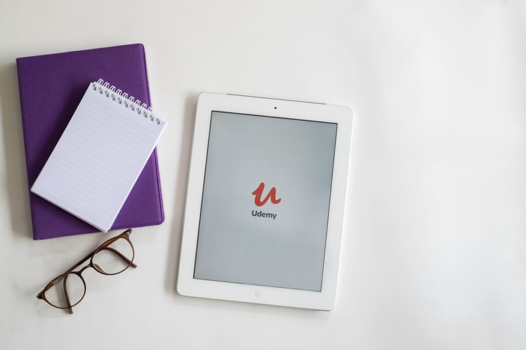 Caderneta e óculos ao lado de um tablet com o aplicativo da Udemy aberto.