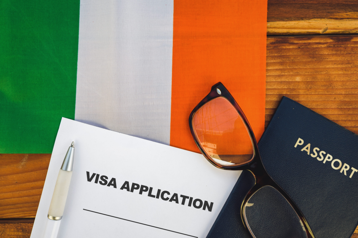 bandeira da Irlanda, passaporte, óculos, folha e caneta em cima da mesa