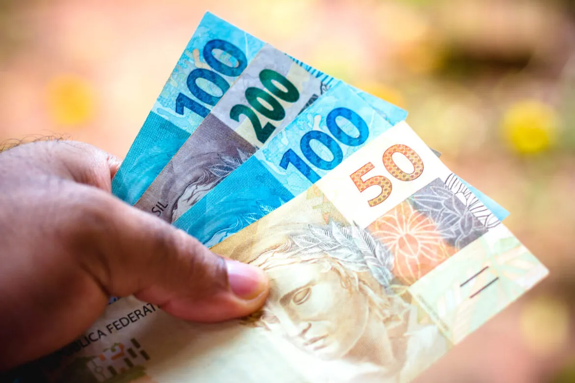 Uma mão segurando notas de 100, 200 e 50 reais