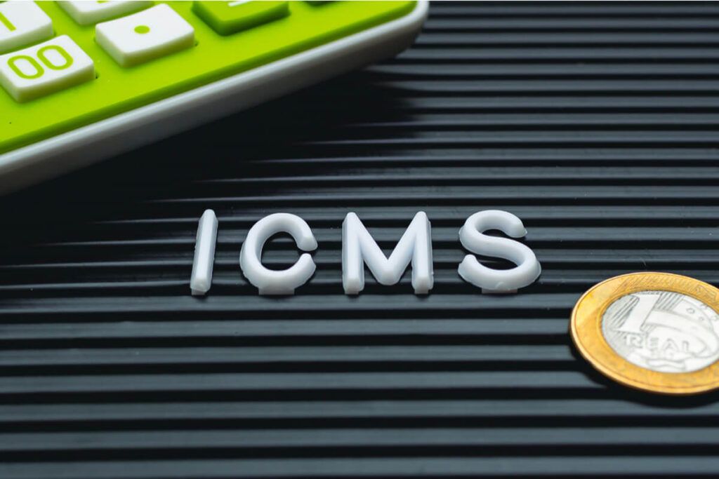 Letras formam a sigla ICMS ao lado de uma moeda de 1 real e uma calculadora