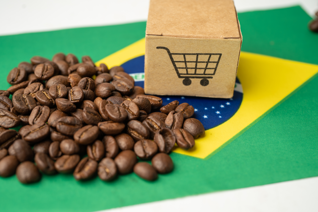 Imagem de grãos de café e uma caixa com a imagem de um carrinho de comprar colocados sobre a bandeira do Brasil