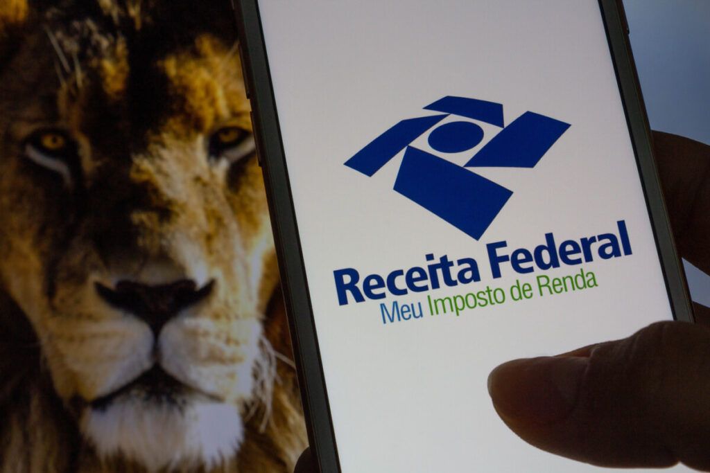 Foto de um celular com o aplicativo da Receita Federal aberto e em segundo plano a imagem de um leão