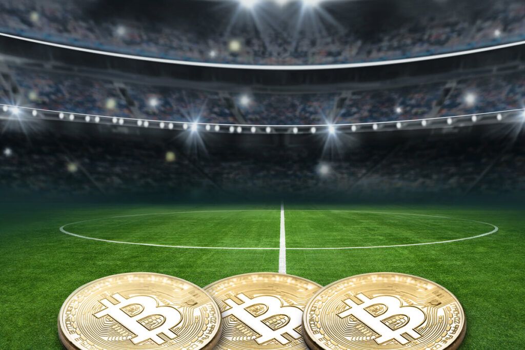 Imagem ilustrativa de moedas de Bitcoin no gramado de um estádio de futebol