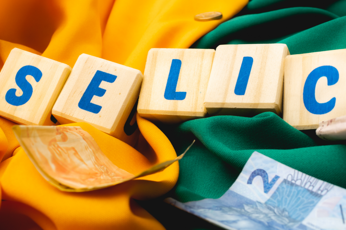 Imagem de blocos que formam palavra SELIC colocados sobre uma bandeira verde e e amarela, com notas de 50 e de 2 reais