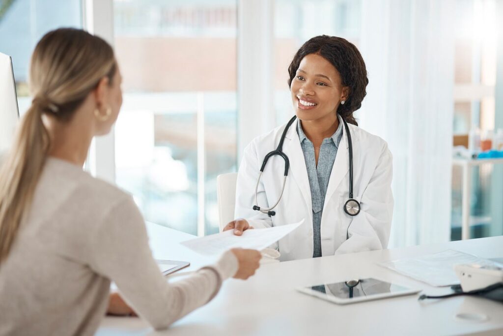 Médica do sistema de saúde em Portugal atendendo paciente no consultório.