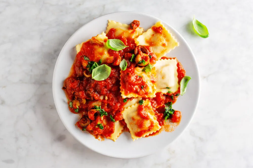 Culinária italiana: ravioli com molho de tomate, queijo e manjericão