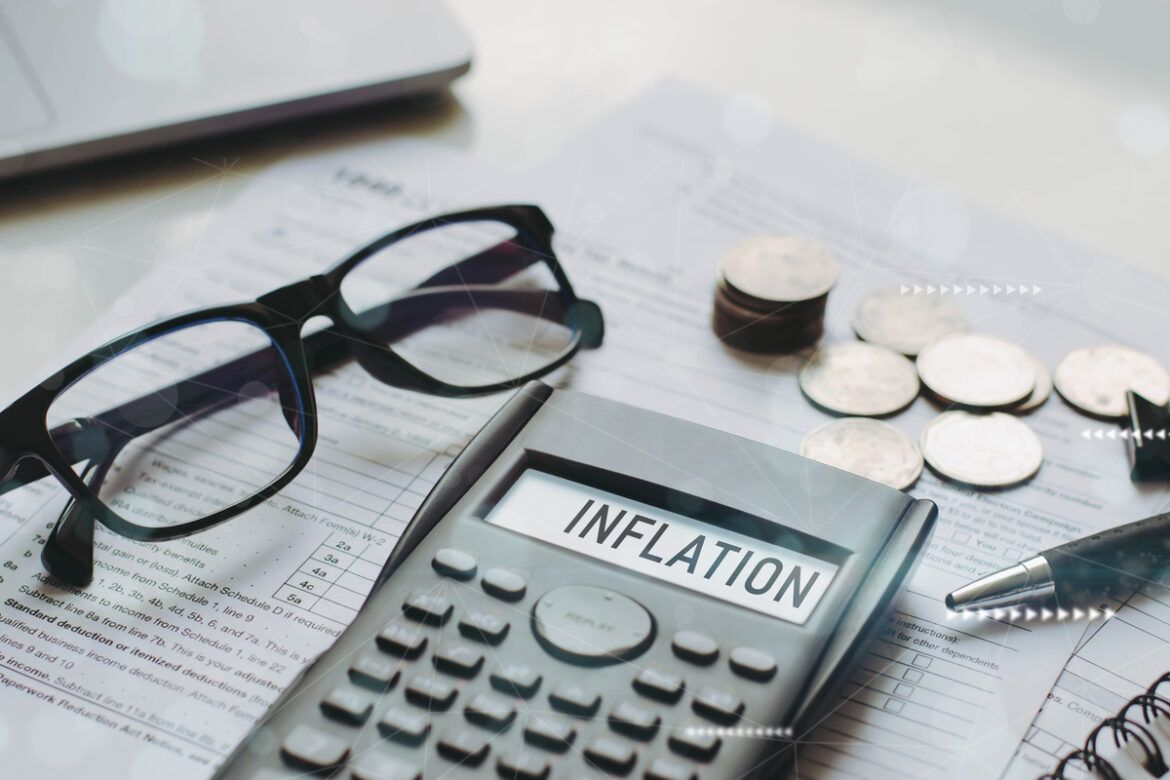 calculadora escrito inflação, óculos, papeis e moedas em cima da mesa