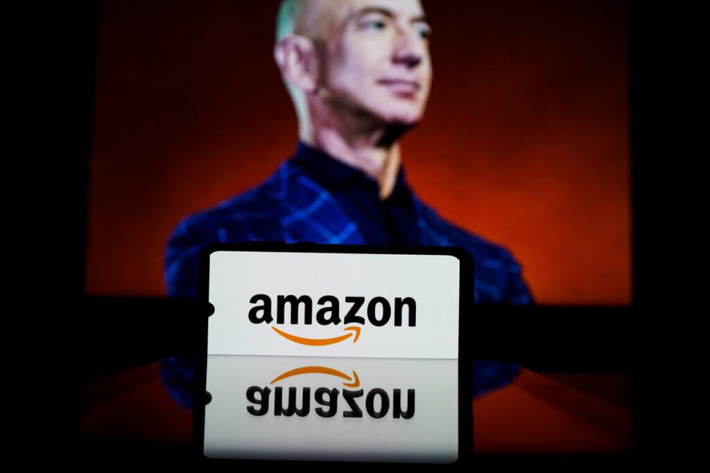 Imagem de um celular com o logo da empresa Amazon e, ao fundo, Jeff Bezos