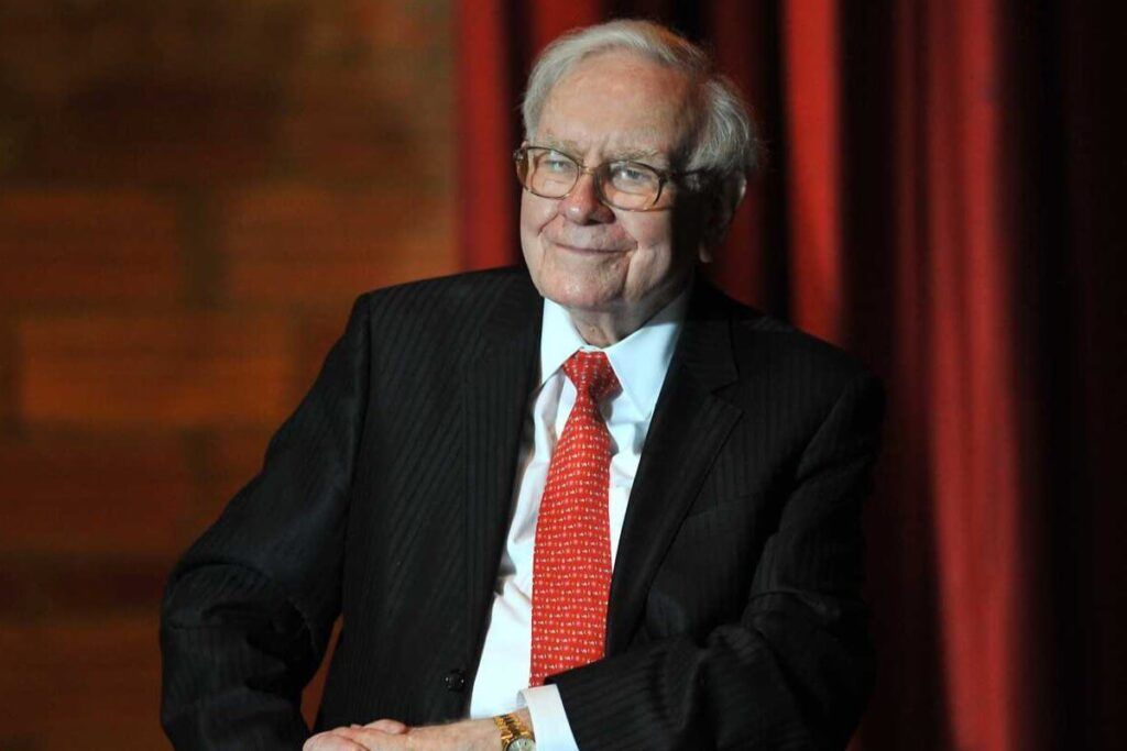 Foto de Warren Buffet em frente à uma cortina vermelha