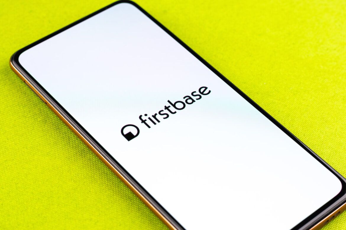 Um smartphone sobre um fundo amarelo com o logotipo da Firstbase na tela