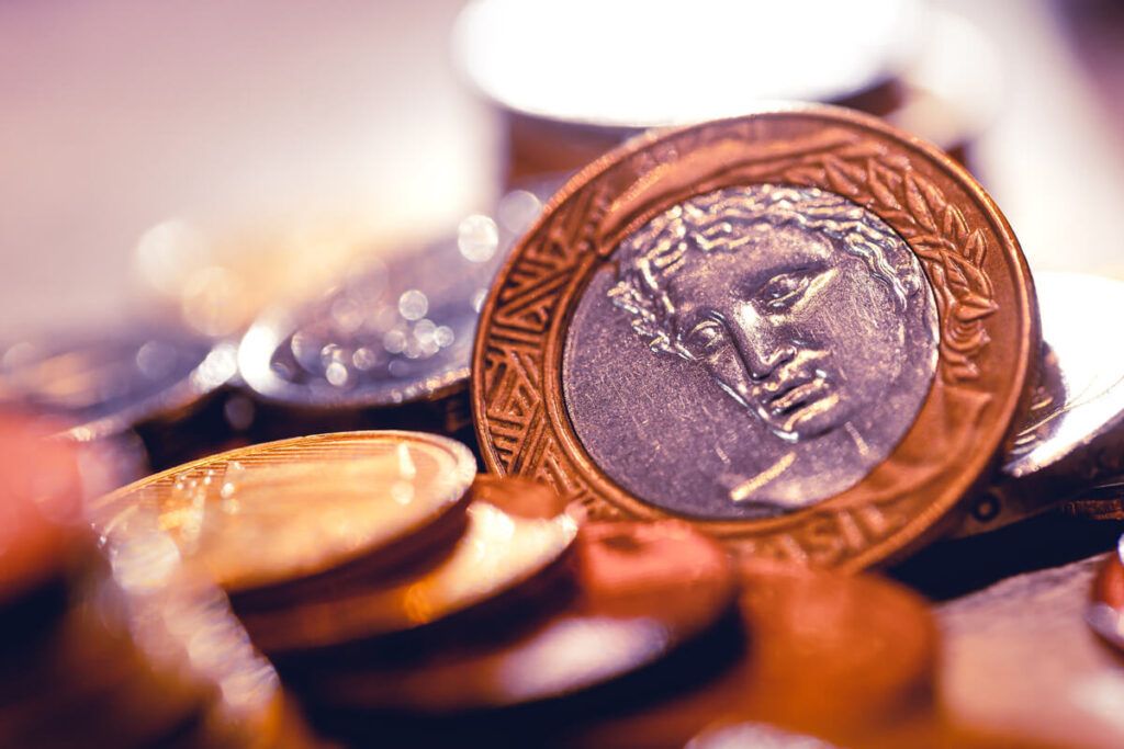 Imagem de moedas amontoadas com destaque para as costas da moeda de 1 real