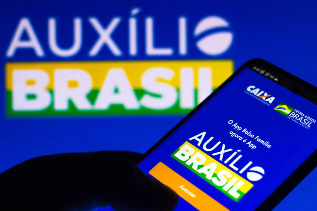 Imagem de um celular com o logo do auxílio Brasil na tela e ao fundo