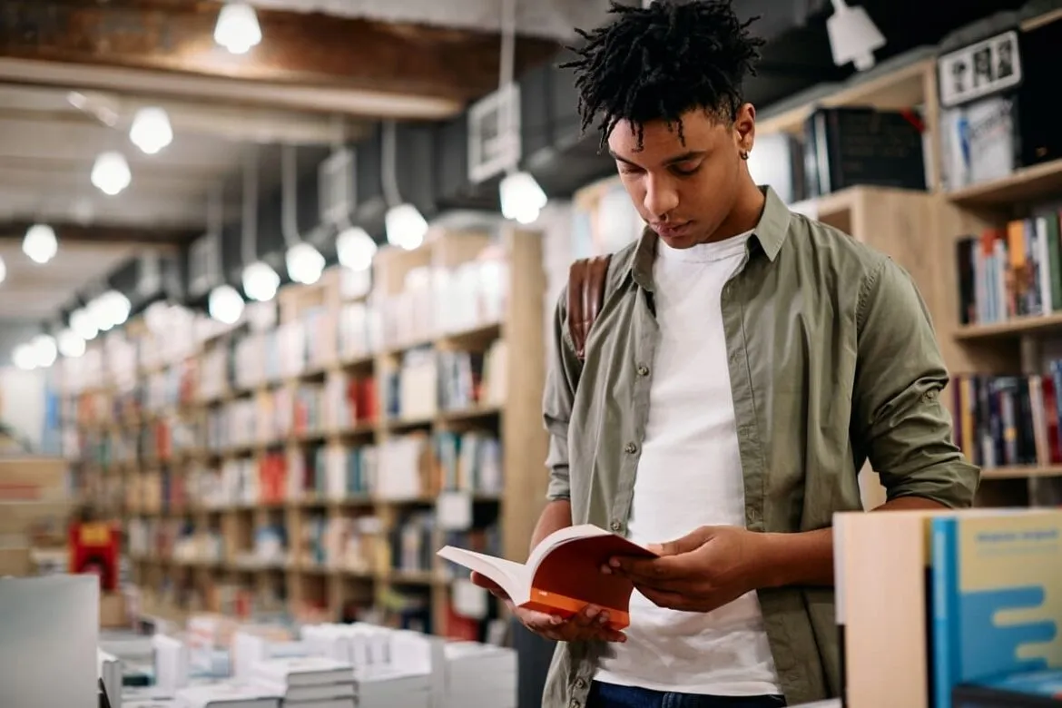 Homem negro pesquisando livros sobre vendas em uma biblioteca.