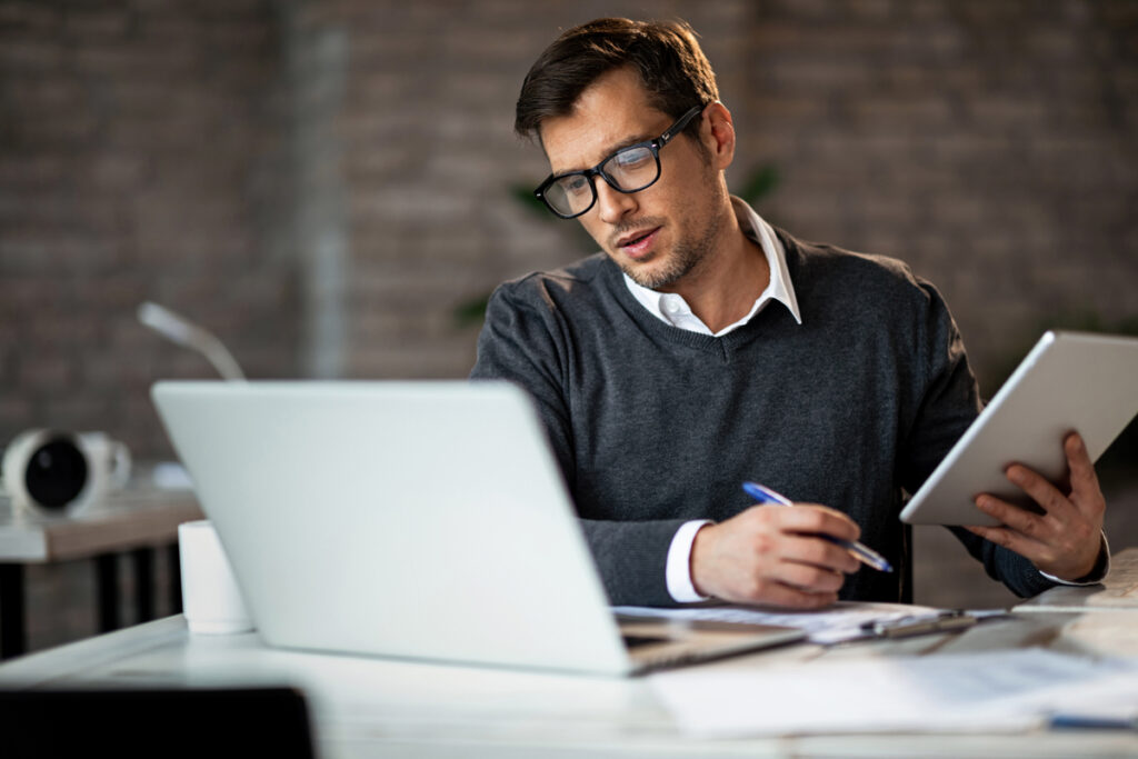 homem segurando um caderno na mão e analisando em frente do computador em como investir na NFT