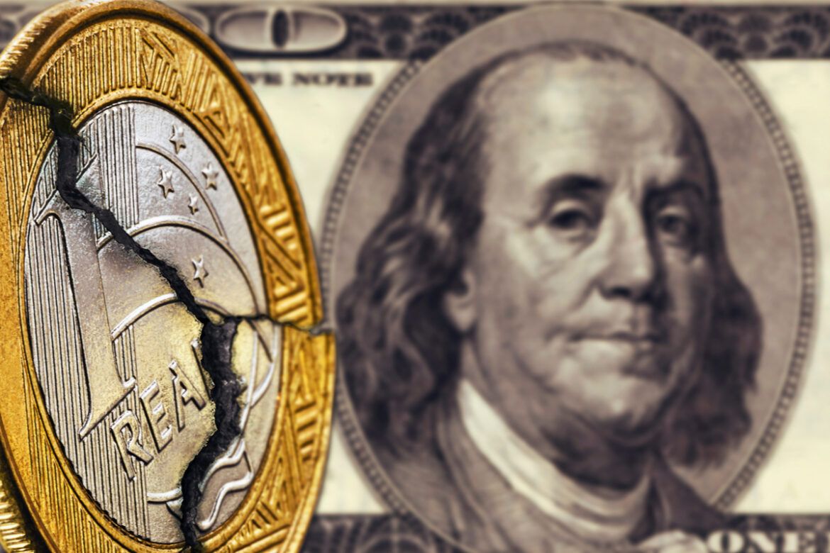 Imagem de uma moeda de 1 real quebrada frente a uma nota de dólar