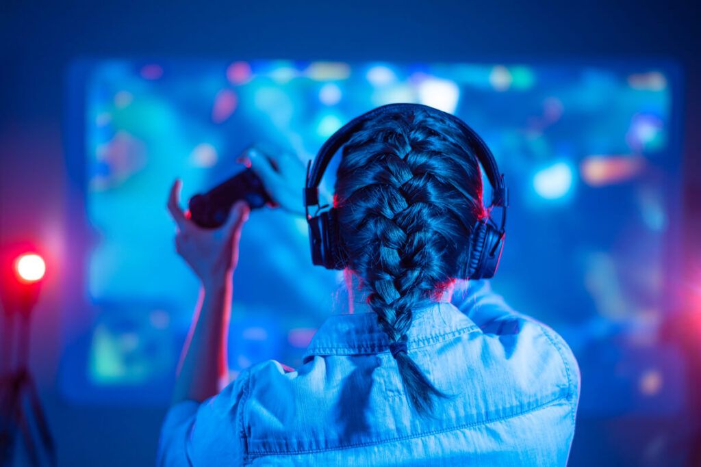 Foto de uma garota com fone de ouvido e um controle de video game em frente à uma TV