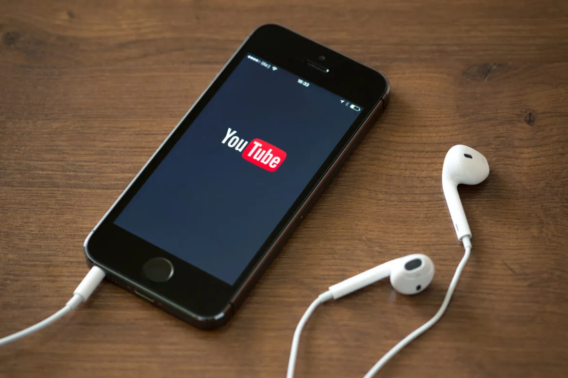 Imagem de um smartphone acessando o YouTube e com fones de ouvido conectados