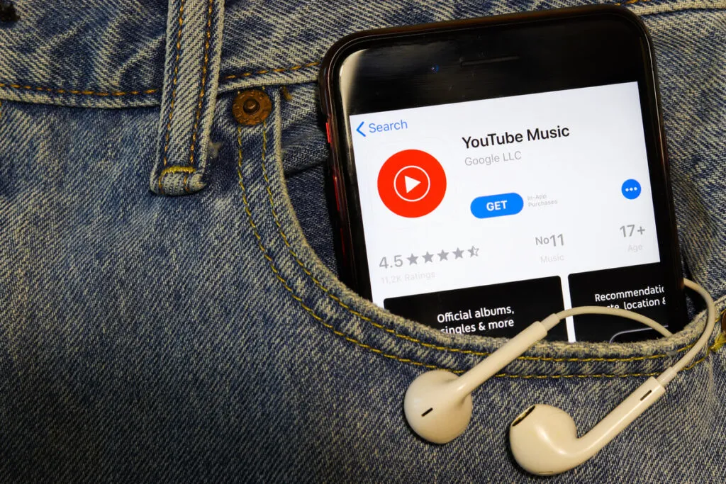 Um celular no bolso de uma calça jeans acessando o YouTube Music, com fones de ouvido conectados